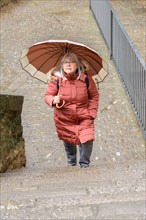 Older woman with coat and umbrella climbing a flight of stairs in a park