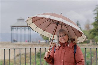 White-haired woman with coat and umbrella on a rainy morning looking at the camera smiling