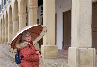 Woman with umbrella and backpack looking at the camera standing in front of stone arches