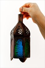 Close-up of a metal lantern with colored crystals held by a woman on a white background