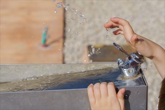Close-up of a child's hands playing with the water jet of a fountain