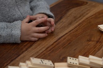 Child's hands in gray sweater playing dominoes with blurred focus