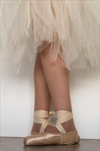 Legs of girl dancing ballet with tulle skirt and pink shoes different dance steps wooden floor and white background with copy space