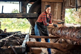 Woman in work clothes carrying a large log in a sawmill