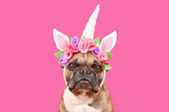 French Bulldog dog wearing unicorn costume headband with flowers in front of pink background