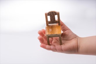 Child holding a brown color wooden toy chair on white background