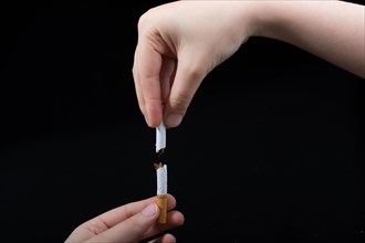 Hand is breaking a cigarette on a black background