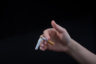Hand is breaking a cigarette on a black background