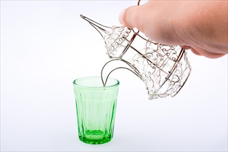 Silver color metal jug over a glass on a white background