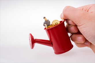 Figurine man standing in a watering can full of fake gold coins
