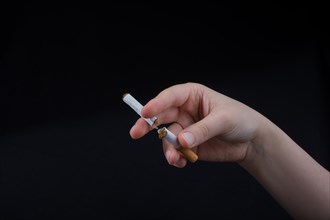 Hand is breaking a cigarette on a black background