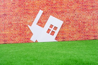 Paper House upside down on red brick background with green grass
