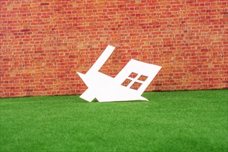 Paper House upside down on red brick background with green grass