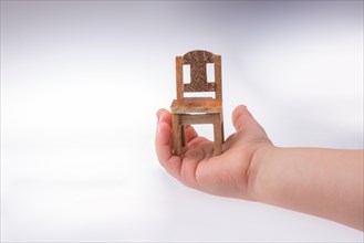 Child holding a brown color wooden toy chair on white background