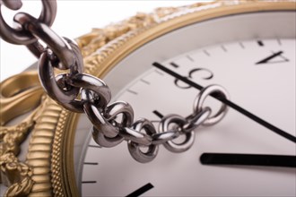 Chain tied to minute hand of a clock and pulled on a white background