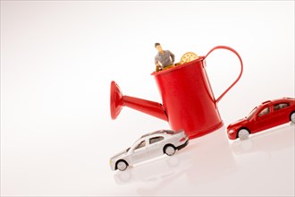 Figurine standing in a watering can with the cars beside