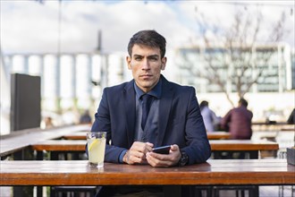 Businessman looking at camera e while holding his smartphone