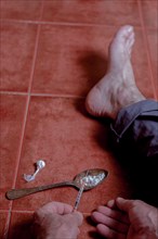 Barefoot man sitting on the floor preparing a drug syringe with a spoon containing heroin