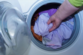 Arm of a woman putting clothes into a washing machine