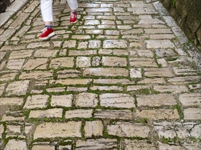 A woman with red shoes walks on a cobblestone street