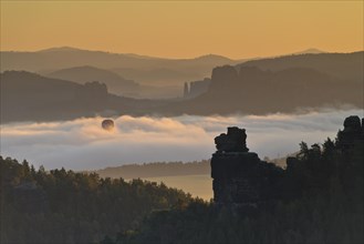 Hot air balloon rising in the morning fog at sunrise in Saxon Switzerland