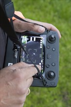 Man operating drone controller with monitor to locate roe deer fawns hidden in grass with thermal imaging camera before mowing grassland in spring