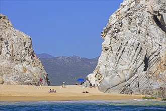 Limestone sea cliffs and tourists sunbathing on secluded beach near the seaside resort Cabo San Lucas on the peninsula of Baja California Sur