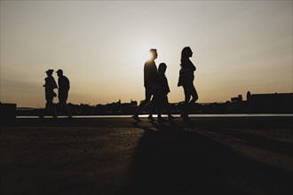Silhouettes of walkers stand out against the setting sun on the harbour promenade in Oslo