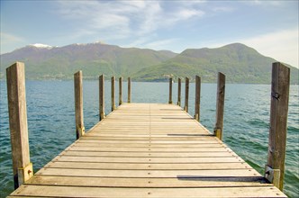Pier over Alpine Lake Maggiore and Mountain with Blue Sky and Clouds in Ticino