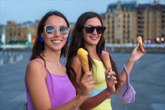Young female friends smiling eating ice cream on summer vacation by the beach