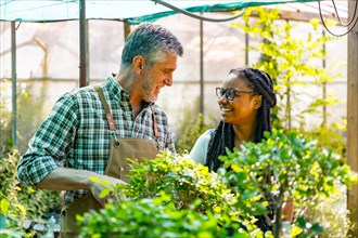Master gardener teaching schoolgirl flower nursery in greenhouse smiling
