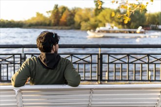 Back view of a man sitting on a bench at sunset contemplating the river
