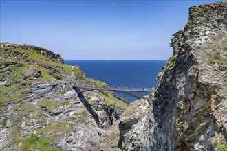 Tourists walk across the new footbridge to the peninsula with the castle ruins of Tintagel Castle