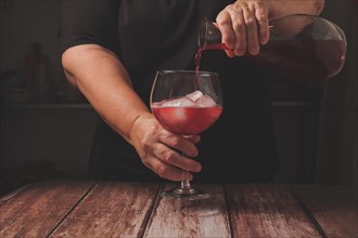 Waitress dressed in black serving a glass of sparkling red summer wine on the rocks from a glass decanter