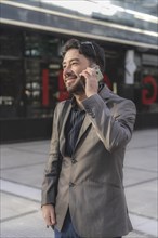Portrait of an attractive smiling businessman talking on the cell phone to a friend outside his office