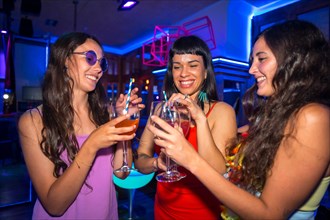Portrait attractive women toasting and having fun with drinks in disco club at summer night party in pub