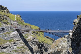 Tourists walk across the new footbridge to the peninsula with the castle ruins of Tintagel Castle