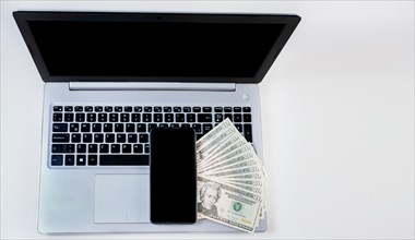 Top view of laptop with cell phone and dollar bills. Cell phone on laptop keyboard and dollar bills. Mobile phone on top of dollar bills on laptop keyboard
