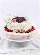 Summery fresh two tier wedding cake decorated with berries and flowers festive cream cake on light background