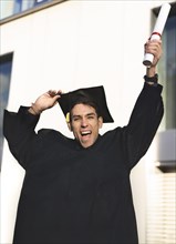 Cheerful smiling graduate man wearing a gown and raising his diploma
