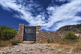 Countryside landscape. Rustic stone wall fence and aged black timber wicket door. Great blue sky with awesome clouds. Concept of closed opportunities