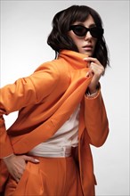 Spectacular beautiful woman in a trendy orange suit with classic make-up. Beauty face. Photo taken in the studio on a white background