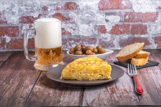 Typical spanish potato omelette freshly made on a wooden table with a fresh pitcher of beer