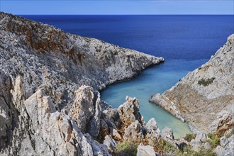 Vertical view of z-shaped cove or bay in typical summer Greek or Cretan landscape on sunny day. Great blue sky and beautiful clouds. Sharp limestone rocks in blurred foreground. Selective focus. Seita...