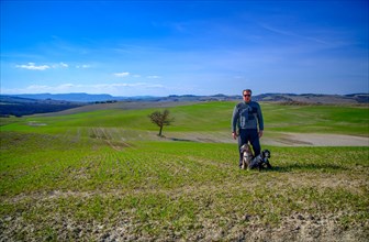 Man with Two Cocker Spaniel Dogs on the Beautiful Agriculture Landscape with a Single Tree in Tuscany