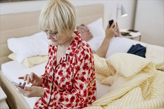 Elderly couple together in the bedroom and each looking at their own smartphone