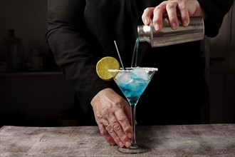 Waiter dressed in black serving a blue cocktail with sugar in the glass and a slice of orange