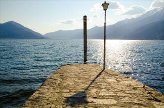 Pier on an Alpine Lake Maggiore with Mountain and Street Lamp with Shadow in Ascona