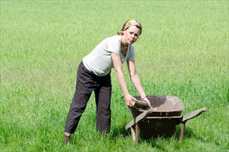 Woman with a Wheelbarrow on the Green Field with Grass