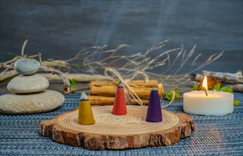 Colorful incense cones on a wooden disk with candles and zen stones stacked on top of them